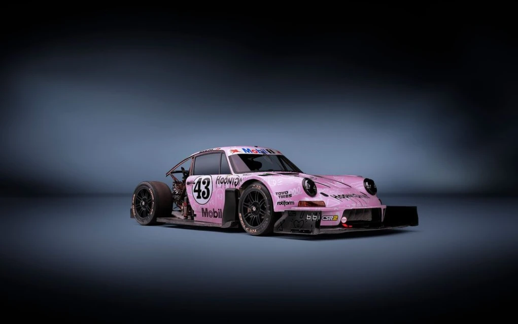 Pink Porsche race car with number 43 and sponsor logos, shot in studio with a dark background, showcasing automotive design and performance.