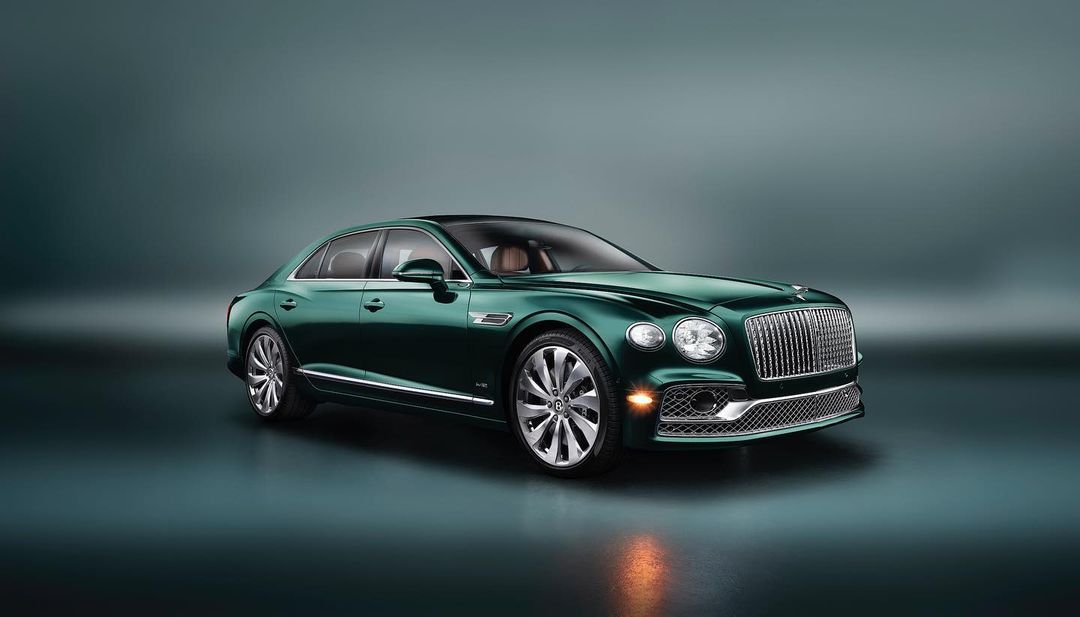 Emerald green Bentley Flying Spur parked on a reflective surface. The luxury sedan showcases its sleek design and elegant features.
