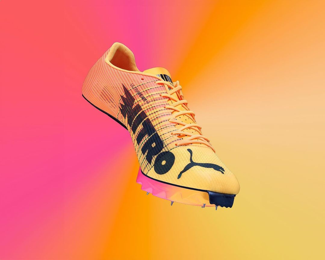 Studio shot of a yellow and orange Puma track shoe with a pink and orange gradient background, showcasing its design and athletic features.