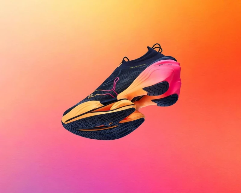 Puma running shoe in floating studio shot. The athletic shoe has a sleek design with a black upper fading to orange at the sole and pink at heel.
