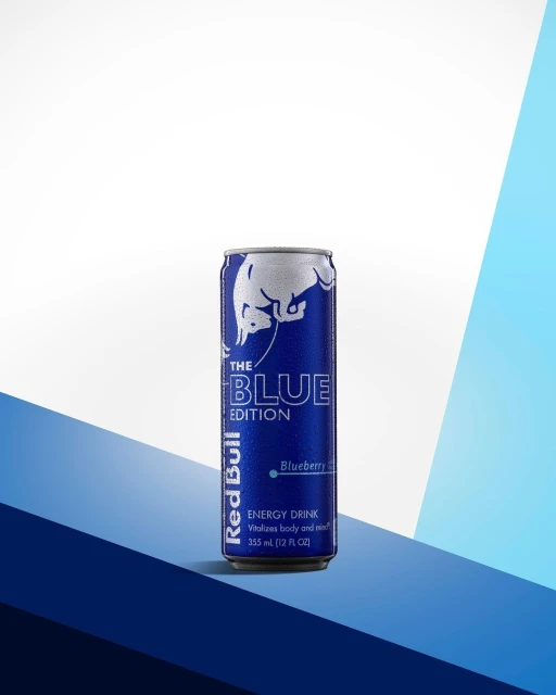 A single can of Red Bull The Blue Edition Blueberry energy drink on a blue and white geometric surface. Clean product shot.