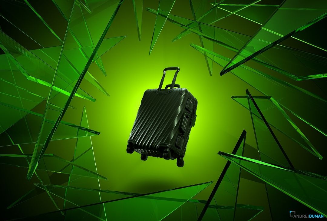 Isolated shot of black rolling suitcase amidst abstract green glass shards against green studio background. Travel and product advertising.