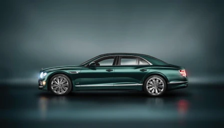 Profile view of a dark green luxury sedan parked in a dimly lit studio with reflective floor and atmospheric fog.