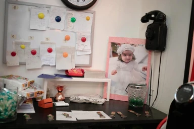 Desk cluttered with papers, receipts, a white board, a framed photograph of a child, and an old black telephone on the wall.