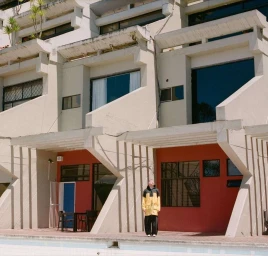 A person standing by a swimming pool in front of a modern brutalist residential building with geometric balconies.