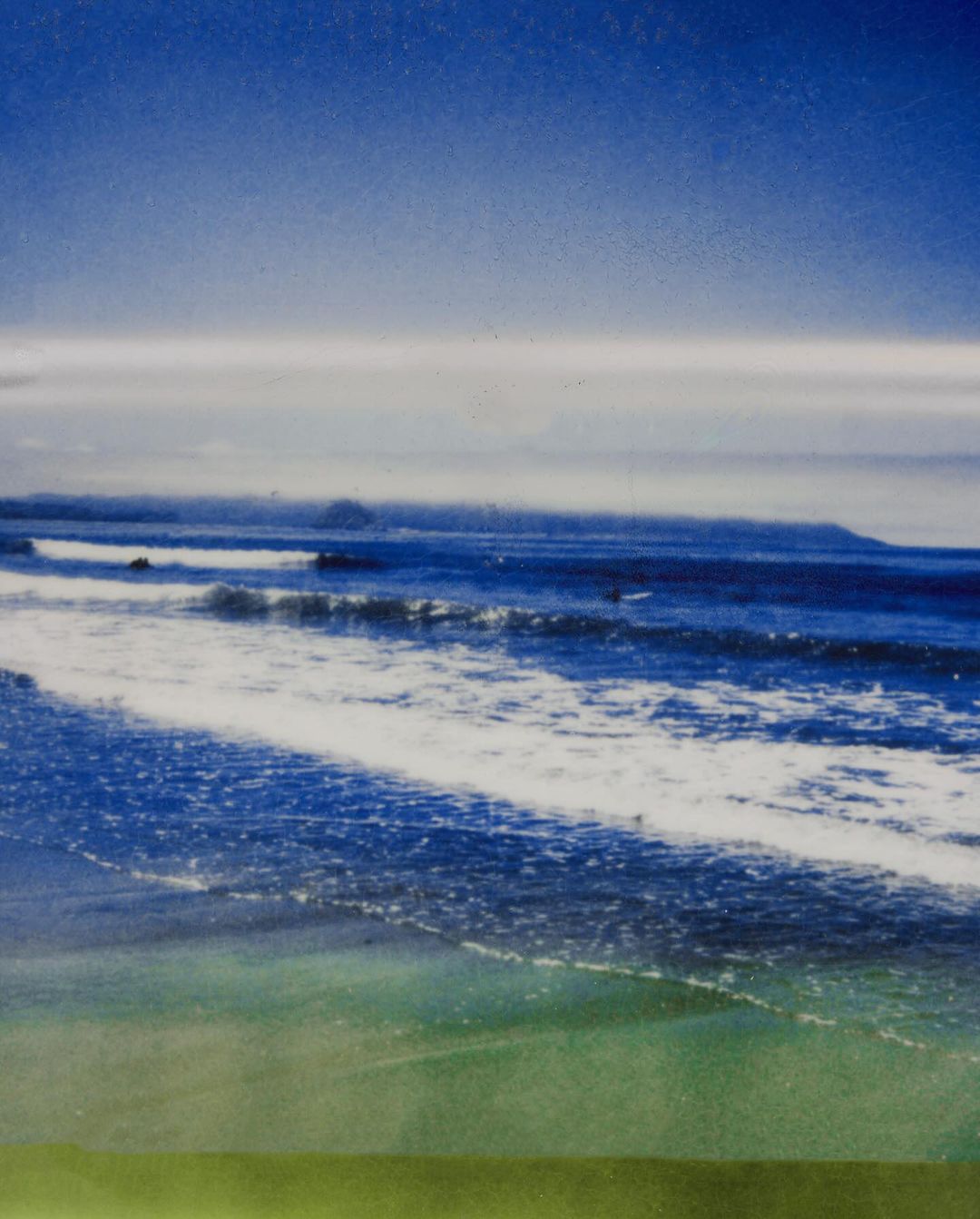 Ocean waves crash on a beach, with a visible shoreline and horizon under a partly cloudy blue sky, creating a serene seascape.