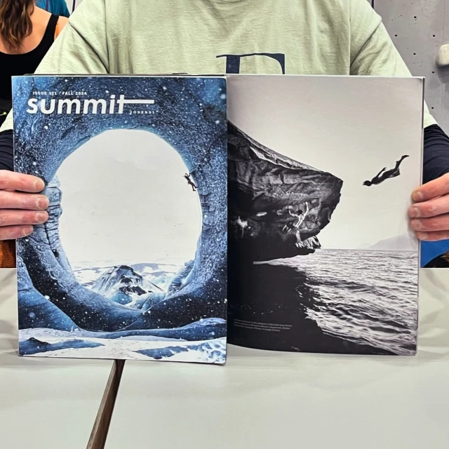 Two magazines featuring nature and adventure photos are held up, including a climber in an ice cave and a cliff diver above the sea.