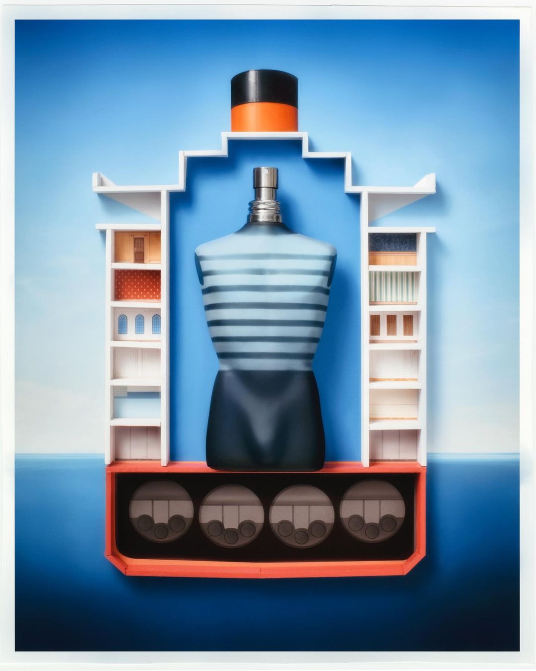 Abstract image of a blue perfume bottle with orange and black cap, presented as an art installation with shelves and patterned compartments.