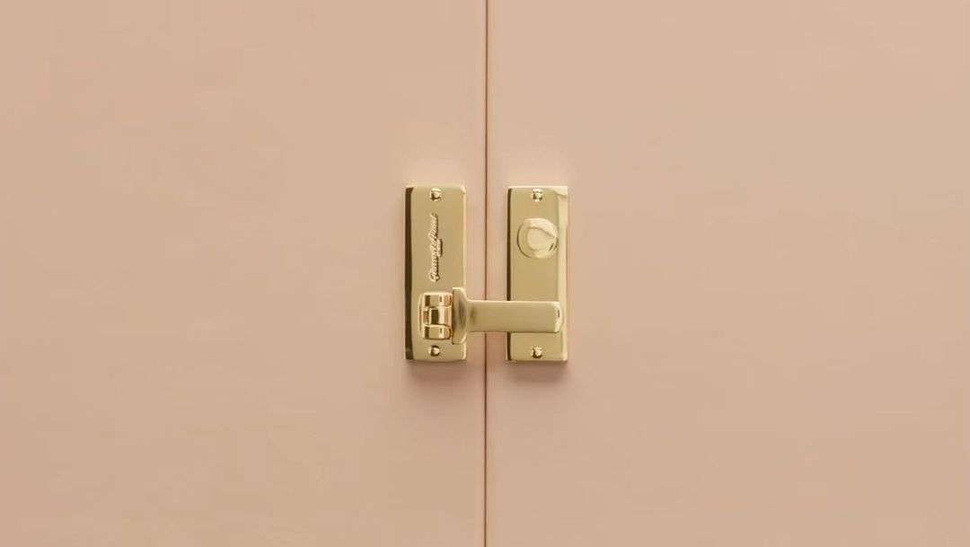 Close-up of a golden door handle with visible brand name on a light pink door. Interior design concept.