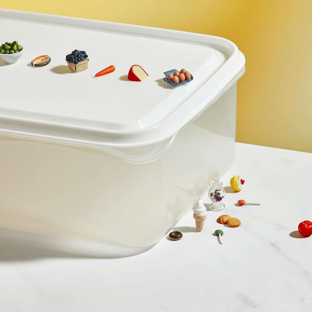 Miniature food models on a white plastic container against a bright yellow backdrop, creating a playful, whimsical scene.