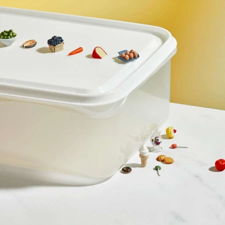 Miniature food models on a white plastic container against a bright yellow backdrop, creating a playful, whimsical scene.