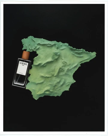 Loewe 001 Man eau de parfum bottle angled on a green map of Spain on a black background. Perfume and travel concept.