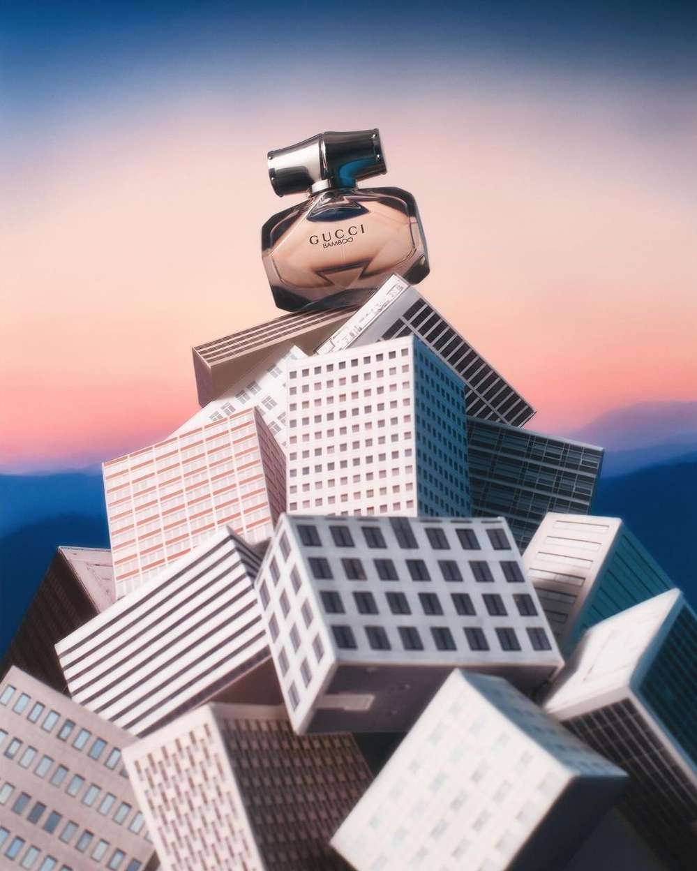 Gucci perfume bottle atop miniature building blocks against a sunset backdrop, product photography for beauty and fashion industries.
