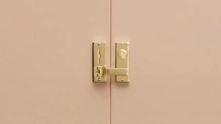 Close-up of polished brass latch and hinge on pale pink double doors photographed by Andrew B. Myers