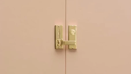 Close-up of polished brass latch and door handle on smooth pink cabinet doors captured by Andrew B. Myers
