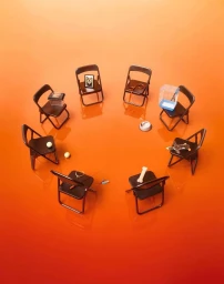 A circle of black folding chairs arranged on a vibrant orange gradient background holding various pet-related objects.