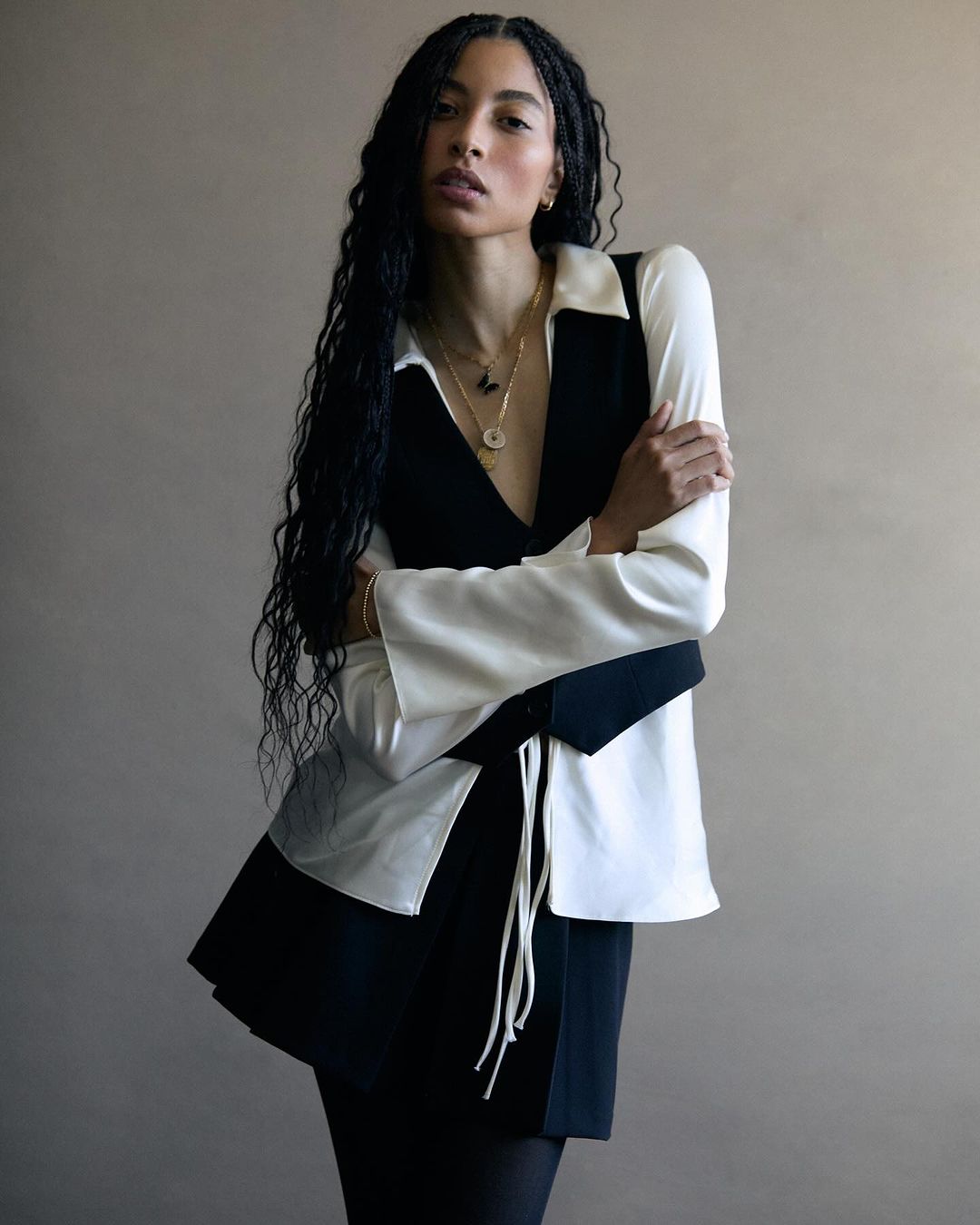 Elegant woman with long dark hair, wearing a black and white vest and skirt, posing against a neutral background in a studio shot.