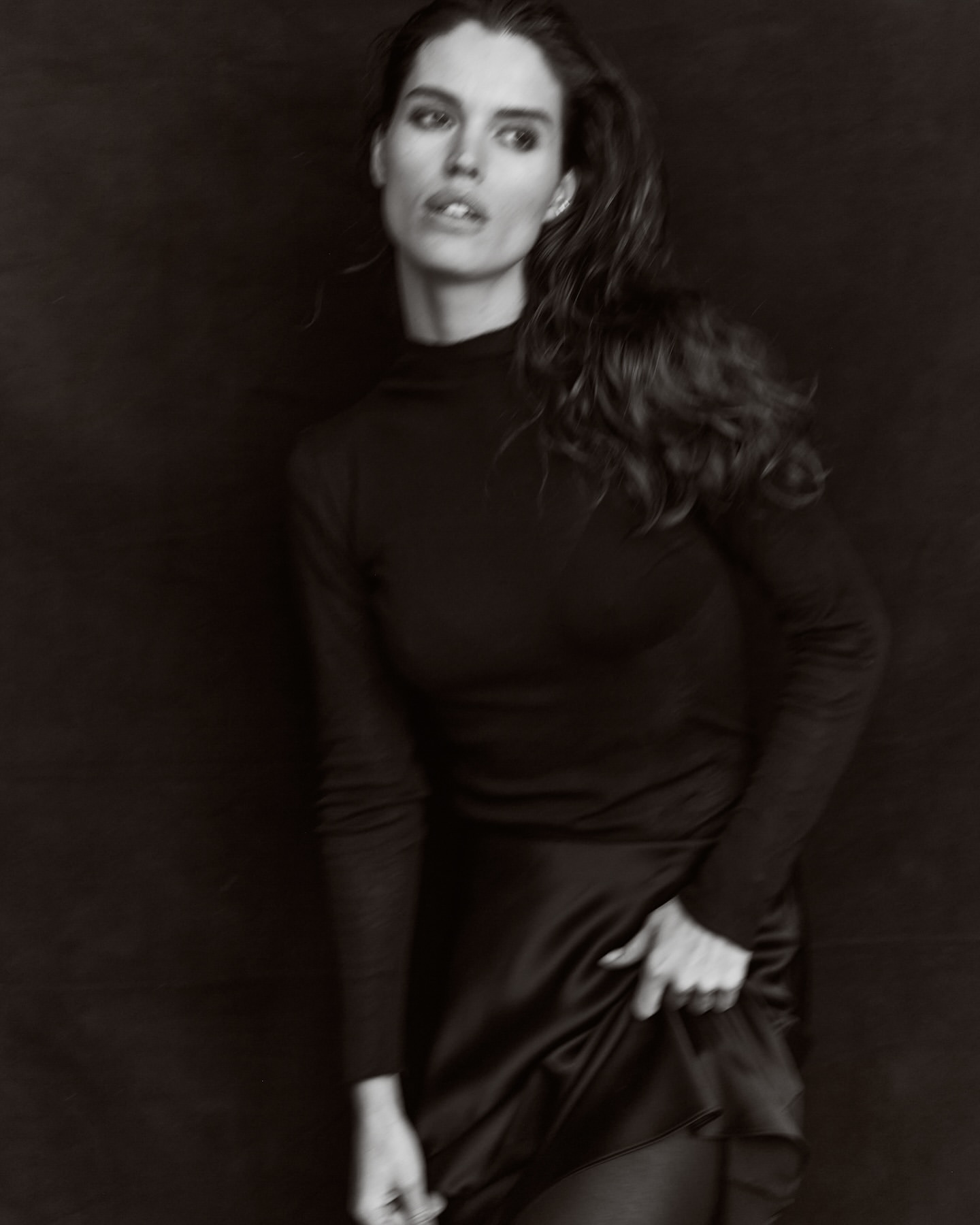 Portrait of a woman wearing a black turtleneck and dark skirt against a dark textured background by photographer Andrew Day