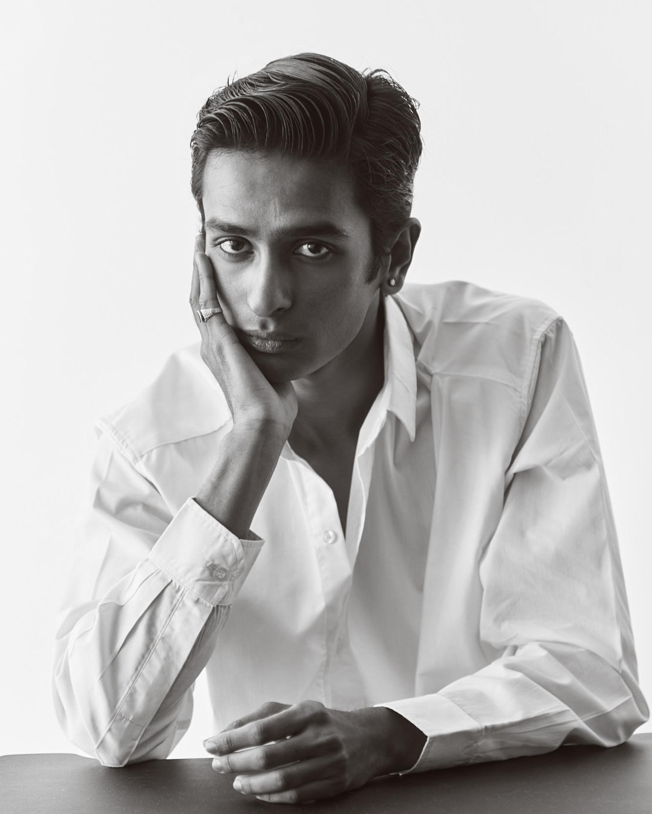 Portrait of a man in a white collared shirt resting his chin on his hand against a plain white background