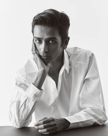 Portrait of a man in a white collared shirt resting his chin on his hand against a plain white background