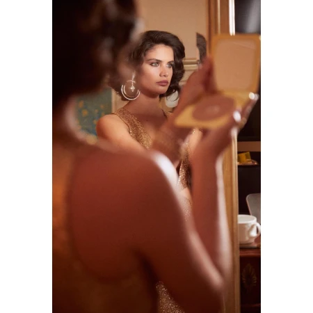 Woman in gold dress holding a compact mirror, reflected in a vanity mirror in New York