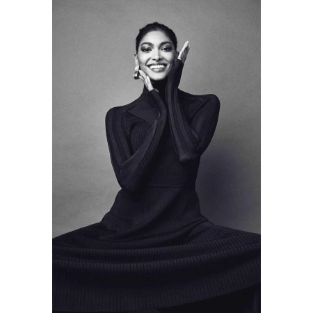 Elegant woman in a black ribbed dress smiles with hands framing her face, creating a striking monochrome fashion portrait.