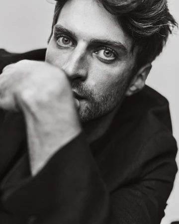 Close-up monochrome portrait of a man with dark hair holding his hand near his face by Andrew Day.