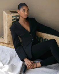 Model in black blazer and trousers sitting among wooden crates on a white cloth backdrop photographed by Andrew Day.