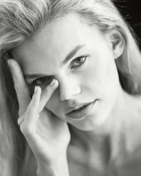 Close-up monochrome portrait of a blonde woman touching her face with hand covering part of her nose.