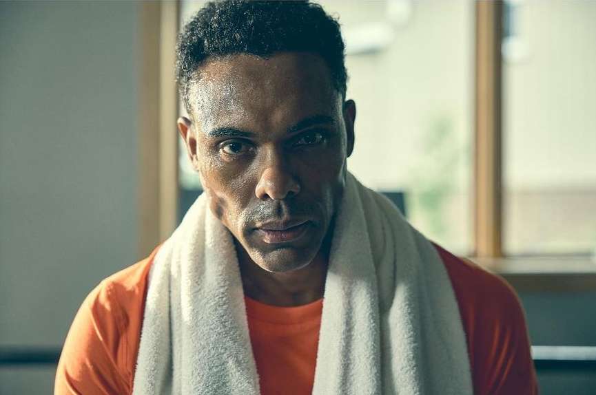 Close-up portrait of a sweaty African-American adult male in an orange t-shirt with a white towel around his neck indoors.