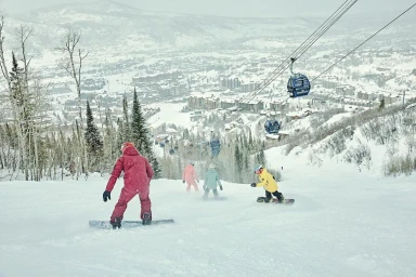 Snowboarders descending a snowy mountain slope with ski lift gondolas visible above them
