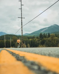 Runner in an orange shirt and black shorts running along an asphalt road with mountain backdrop, photographed by Andrew Maguire.