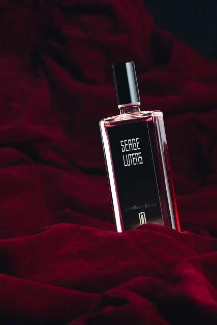 Perfume bottle of Serge Lutens La Fille de Berlin on crushed burgundy velvet fabric in dark and moody studio lighting.