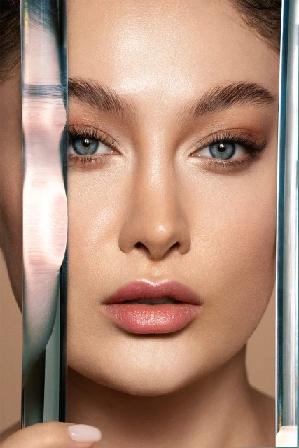 Close-up portrait of an adult female with blue eyes and brown hair, holding a clear rectangular object in a beauty shot.