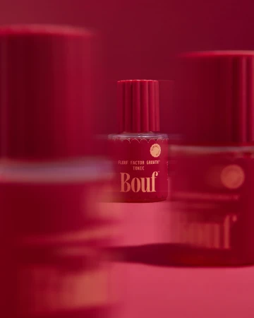 Red beauty tonic bottle by Bouf in sharp focus with foreground and background bottles blurred against a matching red backdrop.