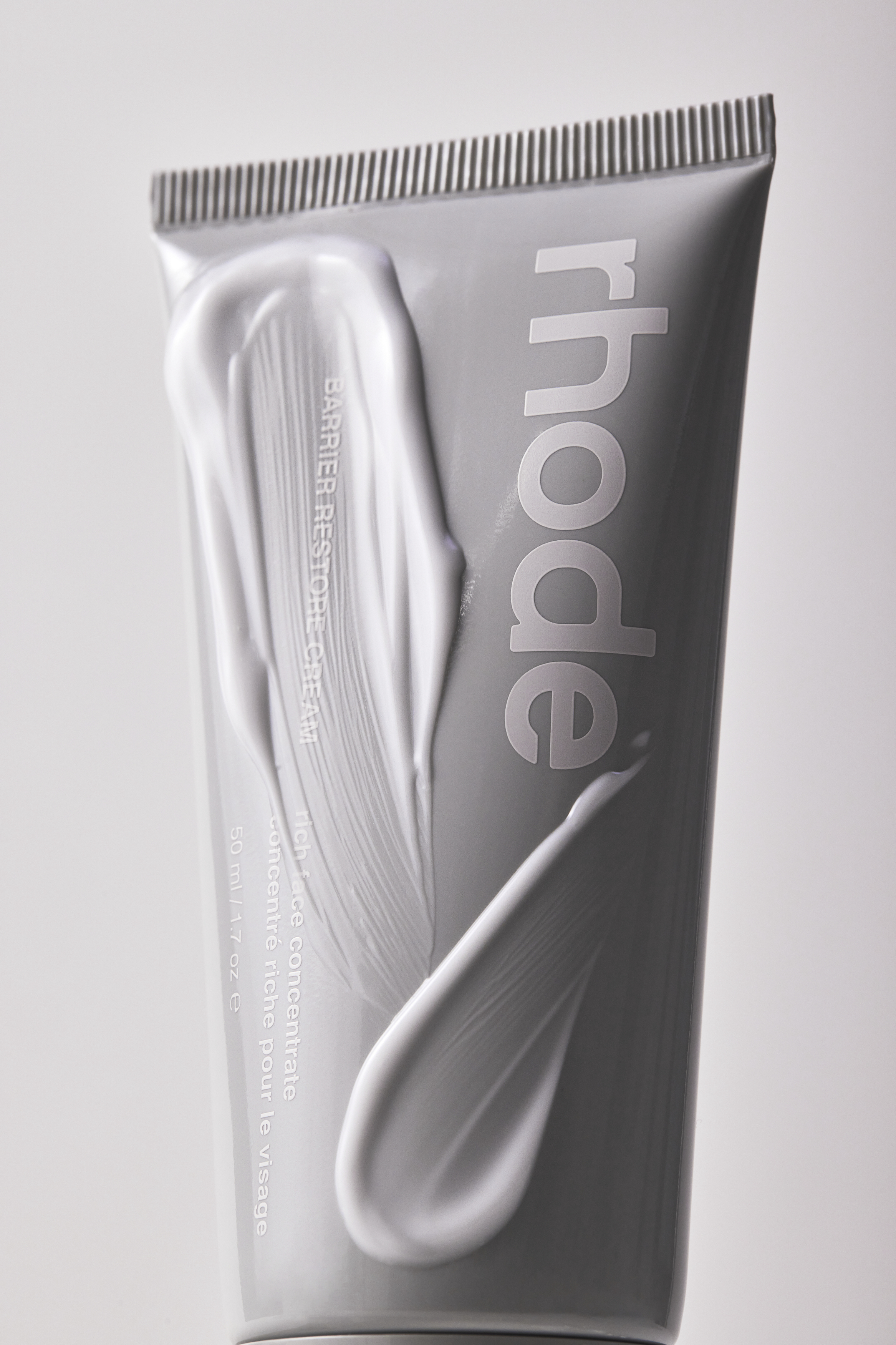 Rhode barrier restore cream grey tube with a thick white cosmetic cream smear on the packaging against a studio background.