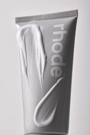 Rhode barrier restore cream grey tube with a thick white cosmetic cream smear on the packaging against a studio background.