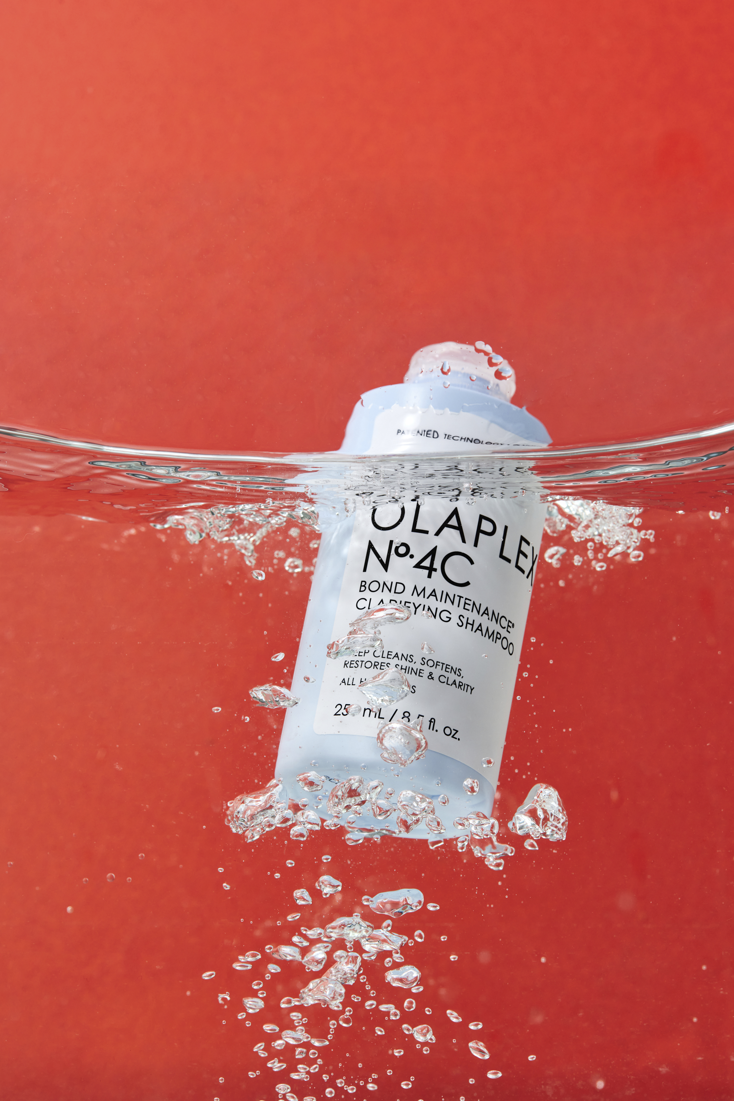 Light blue shampoo bottle submerged in water against an orange background with bubbles