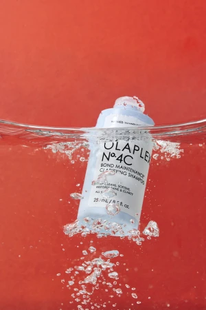 Light blue shampoo bottle submerged in water against an orange background with bubbles