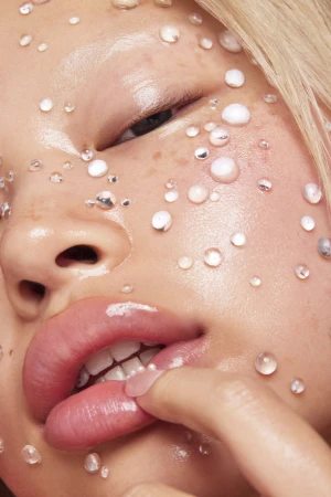 Close-up beauty portrait of an East Asian woman with dewy skin, glossy pink lips, and pearl beads across her face.