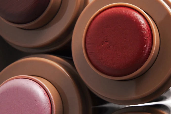 Top-down macro close-up of three cosmetic balm sticks in neutral beige plastic tubes showing red and rose shades.