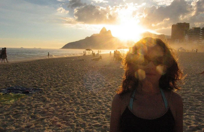Woman in dark top on a sandy beach at sunset with coastal mountains and ocean backdrop