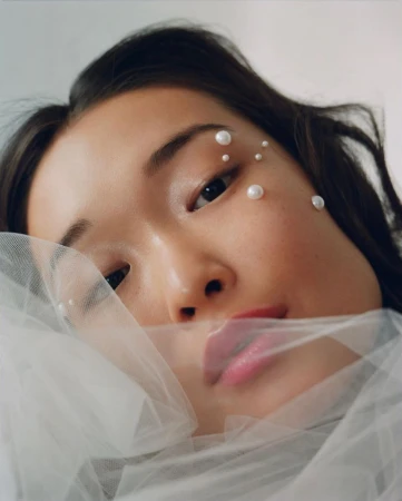 Close up portrait of a young woman with pearl face gems and sheer white tulle draped across her face