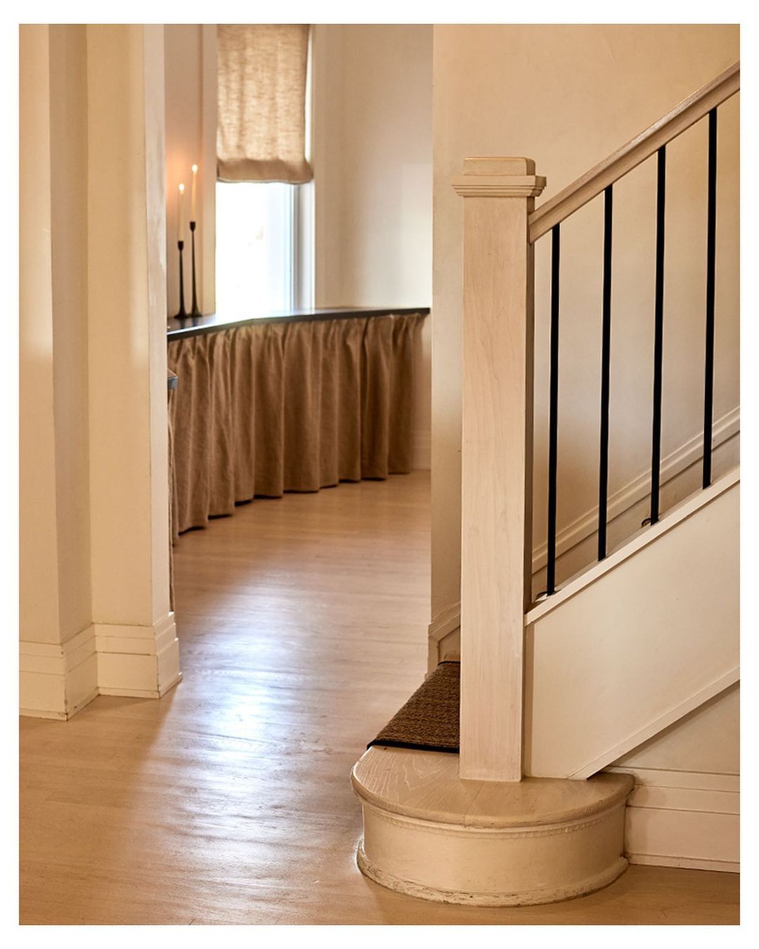 Interior view of a home featuring a staircase with black metal railings, light wood floors, and beige walls with white trim.