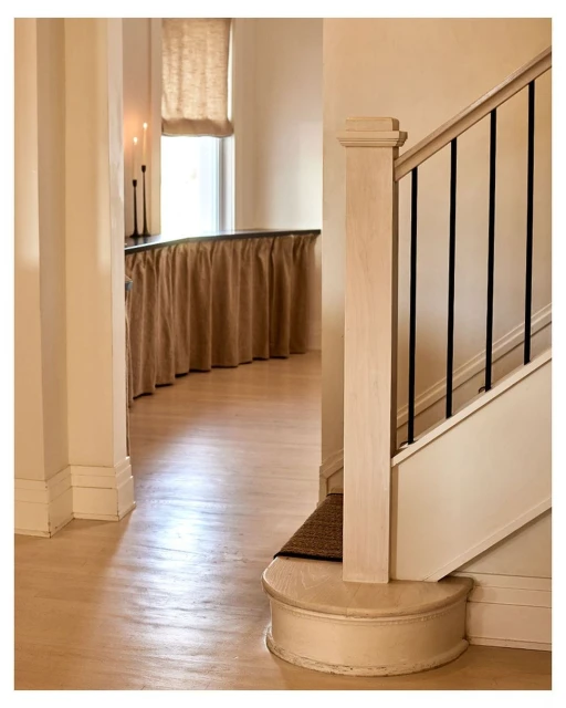 Interior view of a home featuring a staircase with black metal railings, light wood floors, and beige walls with white trim.