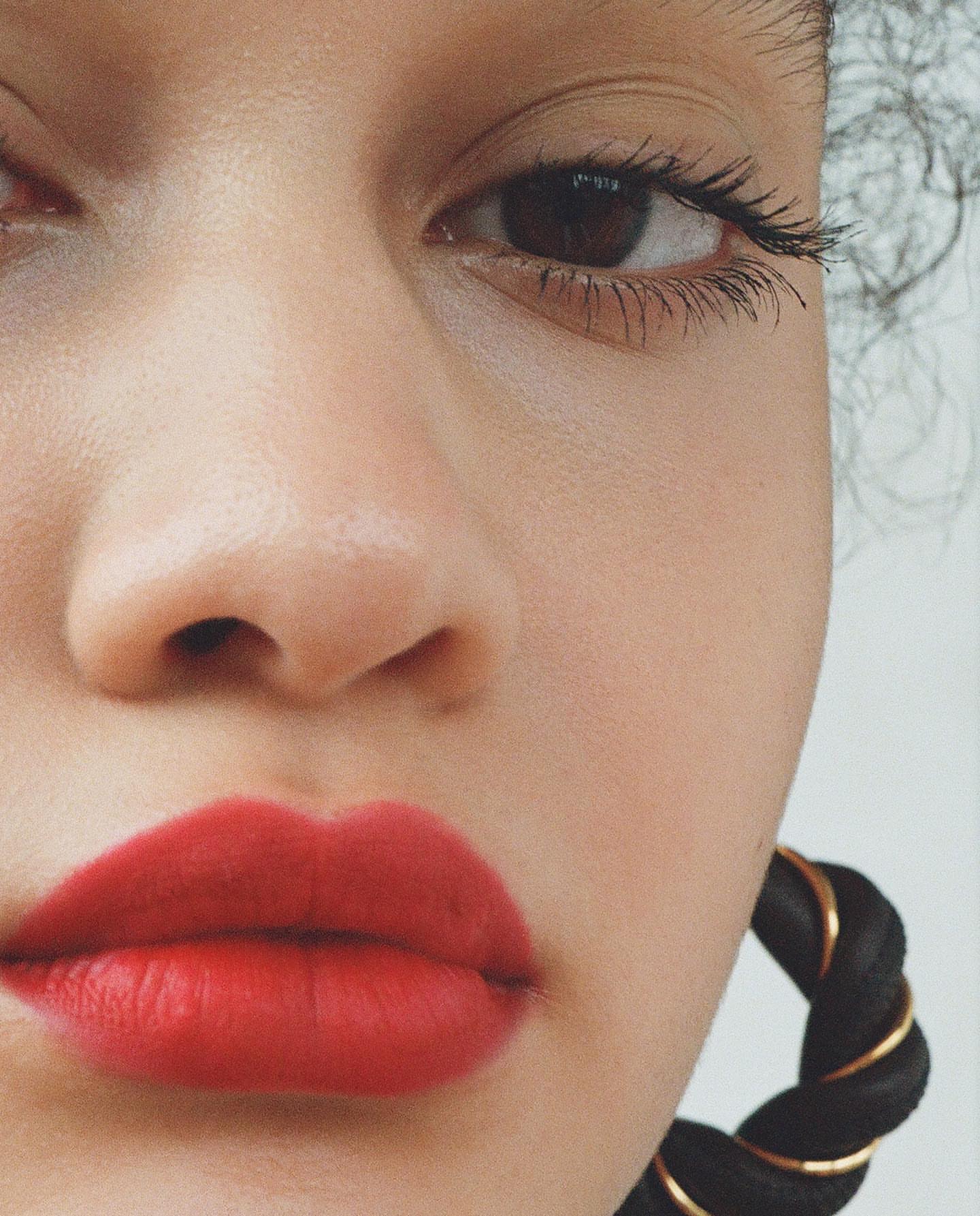 Close-up of a woman's face with red lipstick and a black woven hoop earring featuring gold accents, showcasing beauty and fashion.