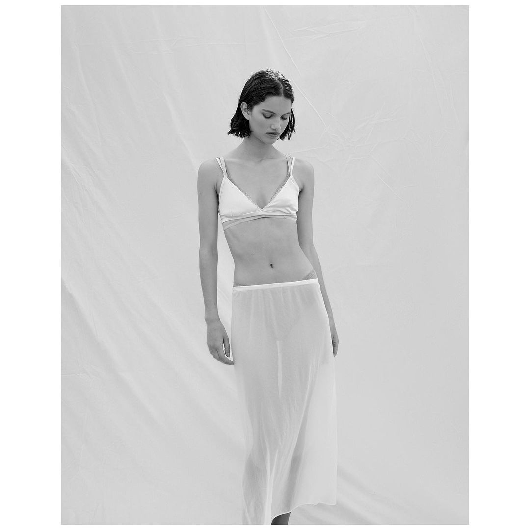 Monochrome portrait of a woman in a bra and skirt against a white backdrop, fashion and beauty photography.