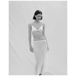 Model in white bra and sheer white skirt standing against a textured backdrop