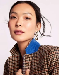 Close-up portrait of an East Asian woman wearing a houndstooth jacket with a blue collar and gold earrings against a light background.