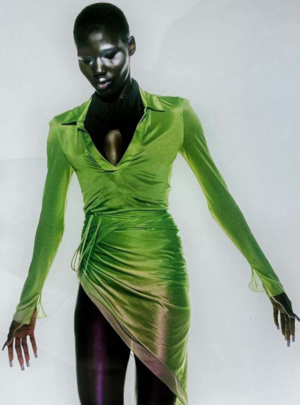 Woman in a vibrant green dress with long sleeves and an asymmetrical hem, set against a pale background. Fashion-forward and elegant.